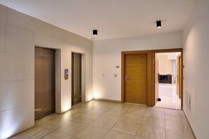 A hallway with two elevators and a wooden door leading to a room. - {The~Urban~Escape}@Downtown Piantini+Gym+lounge (Santo Domingo)