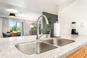 A modern kitchen with a double sink, granite countertop, and a view of the dining area. - Tranquil Golf Themed Getaway with Lake View! (Haines City)