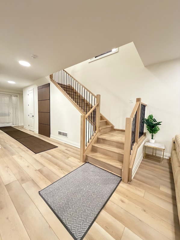 A modern interior with a wooden staircase, a herringbone-patterned rug, and a potted plant.