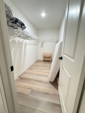 A narrow hallway with a wooden floor, a white door on the right, and a small wooden bench in the center. - Spaciously sleeps 15 in a brand-new 4BR home · Work desks · Minutes to Western (London)