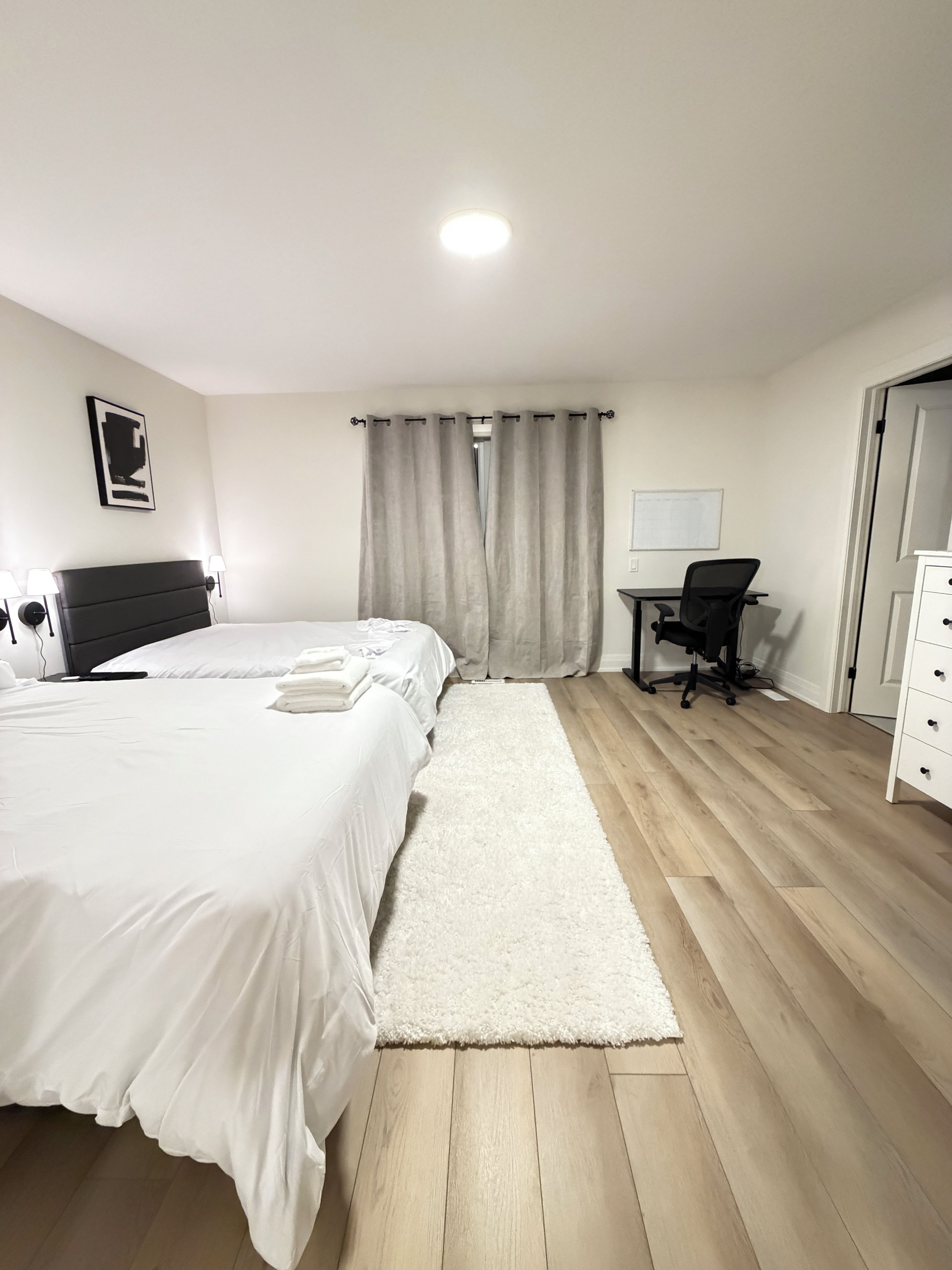Une chambre d’hôtel avec un lit, un bureau, une chaise, une commode et une fenêtre avec des rideaux.