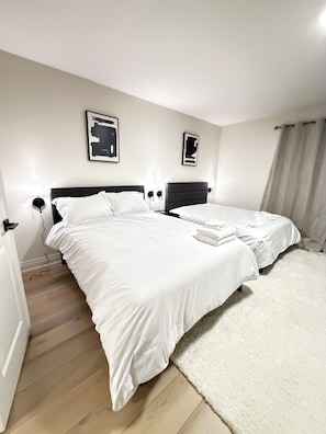 Hotellihuone, jossa on kaksi sänkyä, valkoinen matto ja puulattia.
