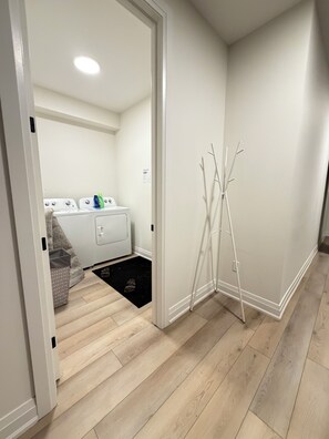 A laundry area with a washing machine, dryer, and detergent bottles. - Spaciously sleeps 15 in a brand-new 4BR home · Work desks · Minutes to Western (London)