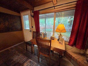 Un coin repas avec une table en bois, des chaises, une lampe et une fenêtre avec des stores.