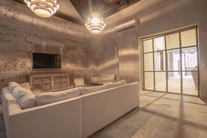 A modern living room with a brick wall, a white sofa, a flat-screen TV, and a large window. - Luxury 8 Bedroom Mansion in Old City Best Location (Cartagena de Indias)
