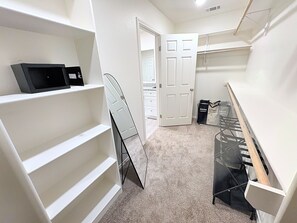 A walk-in closet with white shelving, a coat rack, and a door leading to another room. - Midland Modern 3BR Home (Midland)