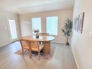 A dining area with a round table, six chairs, a vase with flowers, and a potted plant. - Midland Modern 3BR Home (Midland)