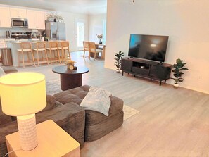 A modern living room with a sofa, a coffee table, a TV, and a kitchen in the background. - Midland Modern 3BR Home (Midland)