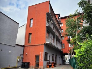 Un edificio de varios pisos con balcones, una entrada visible y un pequeño espacio al aire libre para sentarse.