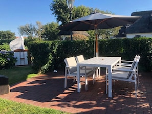 An outdoor patio with a table and chairs, a large umbrella, and a white fence. - Deichhof Holiday Apartment Luana (Dunsum)