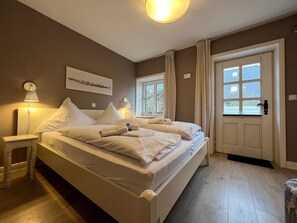 A hotel room with a large bed, bedside lamps, a door with a window, and a wall-mounted artwork. - Deichhof Holiday Apartment Luana (Dunsum)