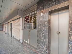 A corridor with closed shop shutters, a marble wall, and a door with a handle. - Deluxe Sri Krishna Palace (Bhubaneshwar)