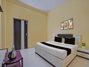 A hotel room with a bed, bedside tables, a chair, a door, and wall art. - Deluxe Sri Krishna Palace (Bhubaneshwar)