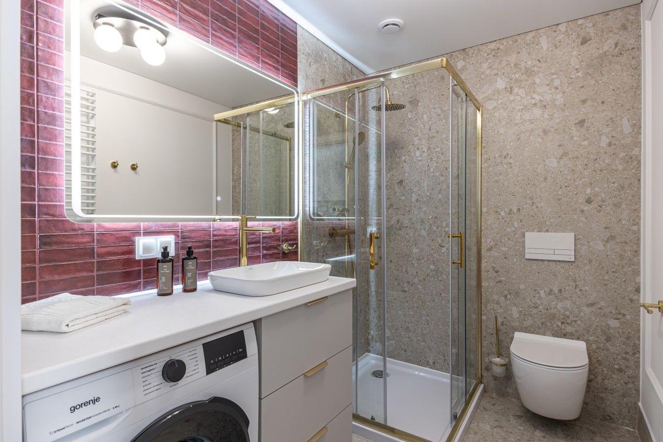 Un baño moderno con ducha de vidrio, lavamanos blanco y lavadora integrada.