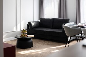 A modern living room with a dark sofa, a round coffee table with fruits, and a dining area with chairs. - Armas 9 Szlachetne Bordo z Sypialni (Bydgoszcz)