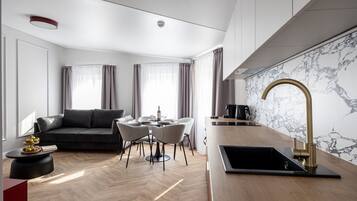 A modern living room with a sofa, dining table, and chairs, a kitchen with a marble backsplash, and a large window with curtains.