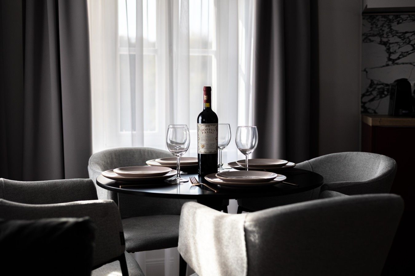 A dining table with a bottle of wine, glasses, and plates set for two.