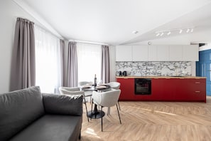 A modern living room with a grey sofa, a dining table with chairs, and a kitchen area with red cabinets and a marble backsplash. - Armas 9 Szlachetne Bordo z Sypialni (Bydgoszcz)