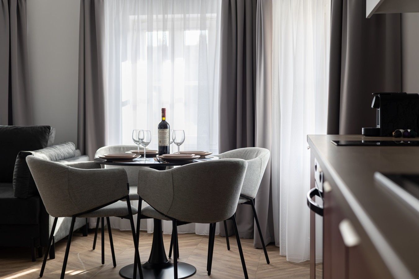A modern dining area with a table set for two, a bottle of wine, and a laptop on a desk.