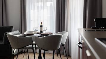 A modern dining area with a table set for two, a bottle of wine, and a laptop on a desk.