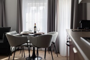 A modern dining area with a table set for two, a bottle of wine, and a laptop on a desk. - Armas 9 Szlachetne Bordo z Sypialni (Bydgoszcz)