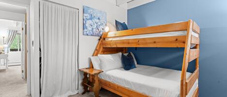 Una cama litera con estructura de madera, ropa de cama blanca y una mesita de noche con lámpara.