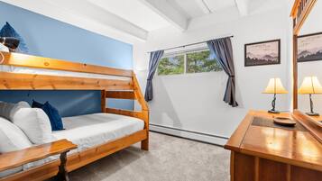 A bunk bed with a desk and lamp, a window with curtains, and a wall with a framed picture.