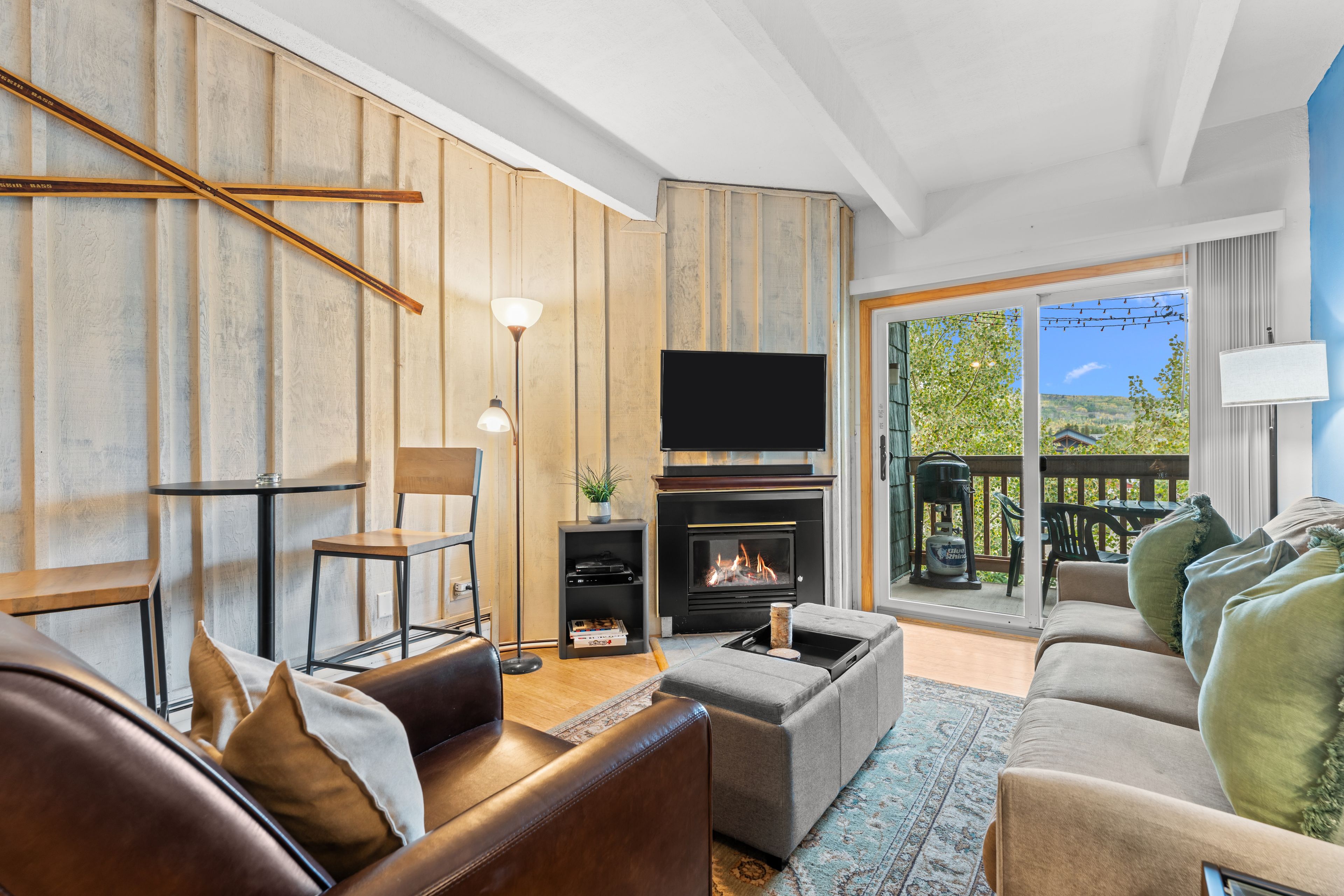 A living room with a fireplace, a sofa, a television, and a view of the outdoors.