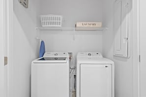 A laundry room with two white washing machines, a blue iron, a white laundry basket, and a shelf with a 'Laundry' sign. - 6BR Themed Villa Private Pool Near Universal (Orlando)