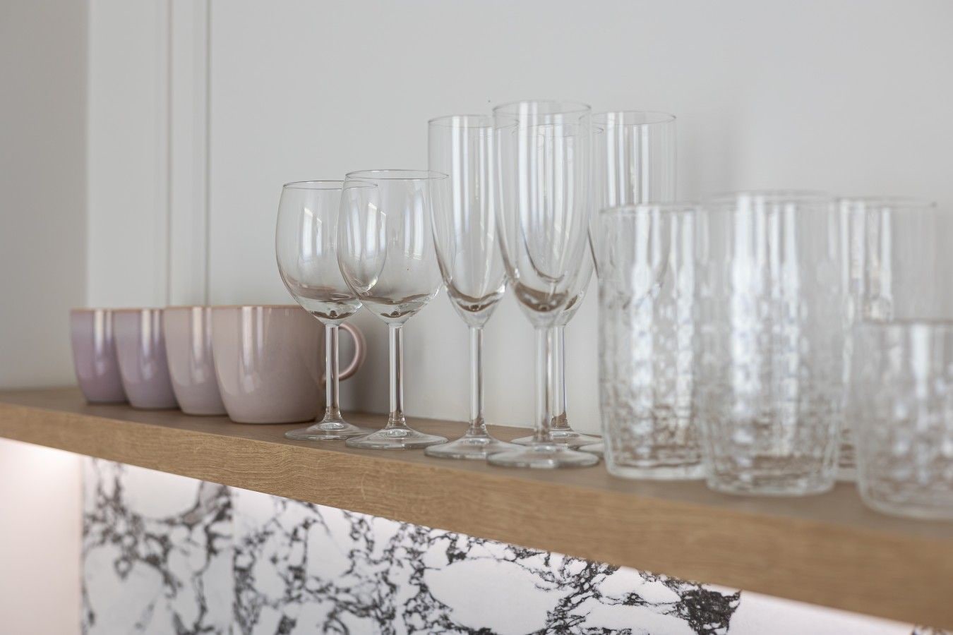 A shelf with clear glassware and ceramic mugs.
