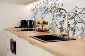A kitchen with a wooden countertop, a black sink, a three-tiered fruit stand, and a marble backsplash. - Armas 5 Granatowa Elegancja z Klimatyzacj (Bydgoszcz)