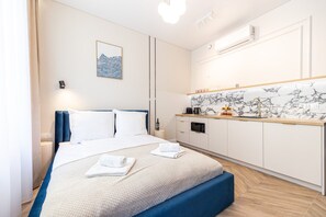 A modern hotel room with a bed, a bedside table, a small kitchen area, and a wall-mounted air conditioning unit. - Armas 5 Granatowa Elegancja z Klimatyzacj (Bydgoszcz)