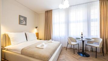 A hotel room with a large bed, a dining table with chairs, a chandelier, and a painting on the wall.