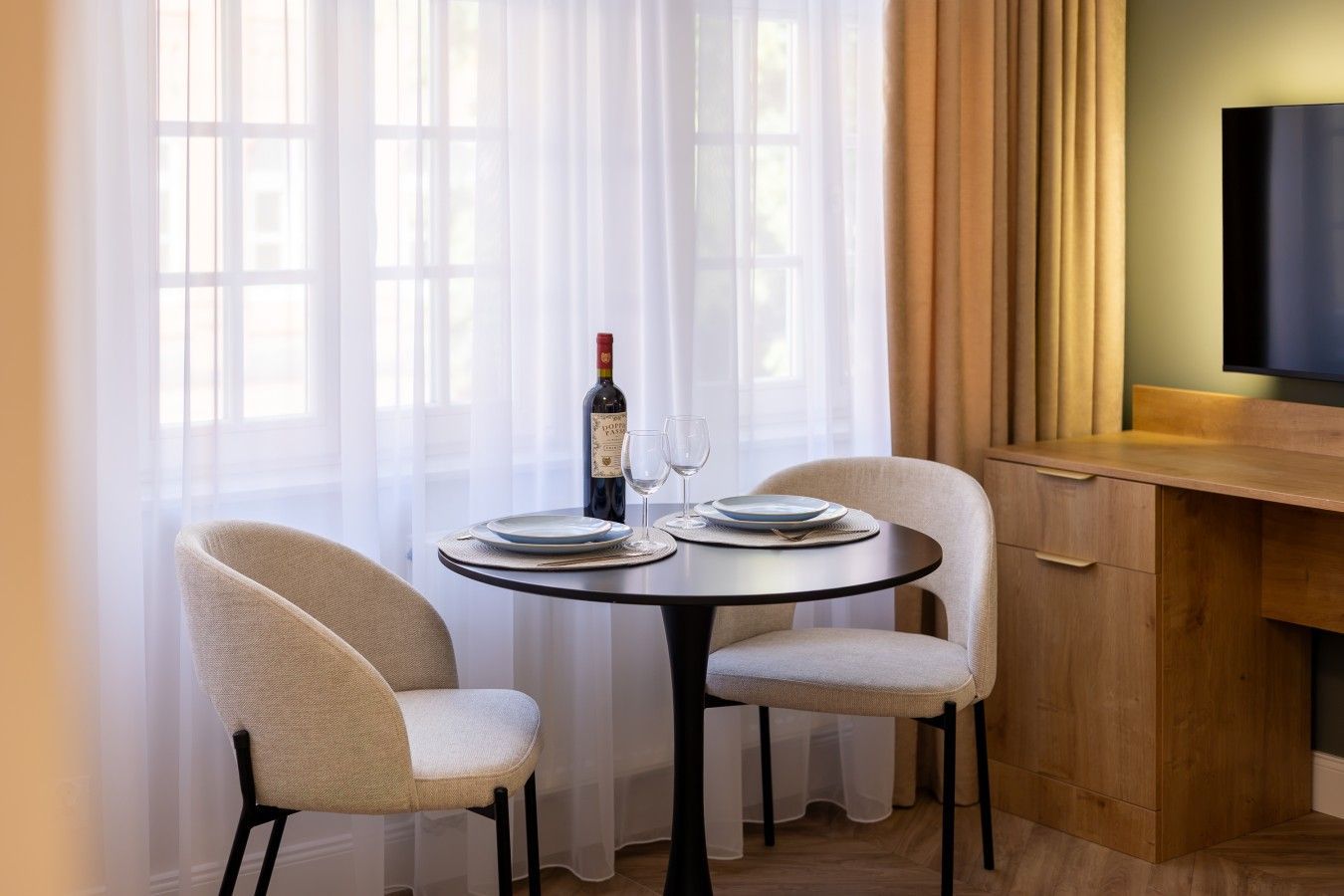 A dining area with a round table, two chairs, a bottle of wine, and a glass.
