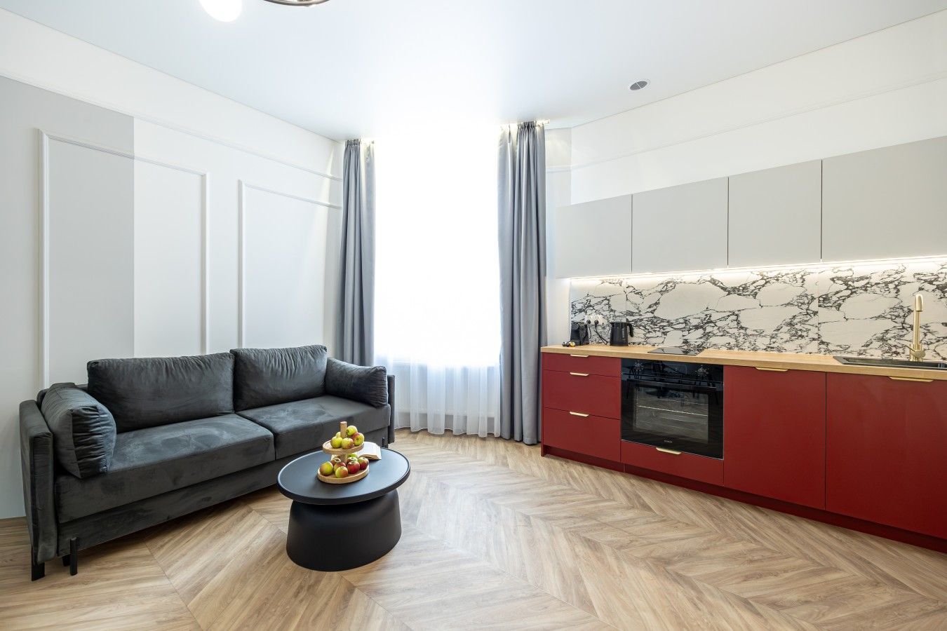 Een moderne woonkamer met een bank, een salontafel en een keukenhoek met rode kasten en een marmeren achterwand.