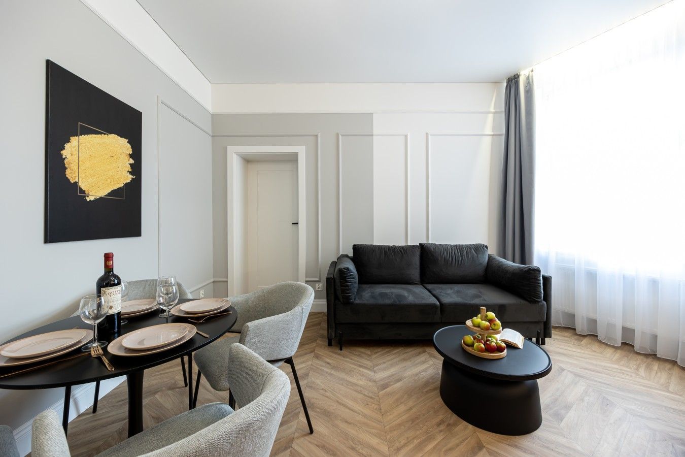 Una sala de estar moderna con comedor, un sofá negro y una mesa de centro con fruta.