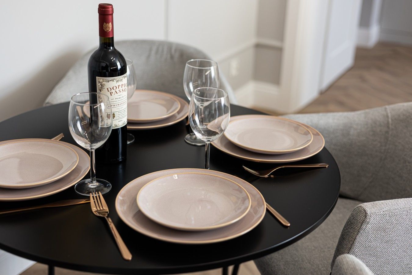 Mesa de jantar posta com pratos, copos, talheres e uma garrafa de vinho.