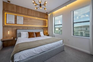 A modern bedroom with a large bed, a wooden headboard, bedside tables, and a ceiling light fixture. - 8BR Themed Villa Pool, Game Room & Theater (Orlando)