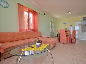 A living room with a sofa, a glass coffee table with a plant, and a dining area with chairs and a table. - Apartments Naplovac (Blato)
