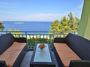 A balcony with wicker furniture, a glass table, and a view of the sea. - Apartments Naplovac (Blato)