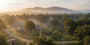 Ländliche Landschaft mit mehreren Gebäuden im traditionellen Stil, umgeben von dichtem Grün und Hügeln im Hintergrund.