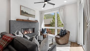 A modern living room with a fireplace, leather sofas, and a large window offering a view of a mountain.