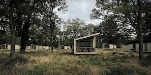 A modern cabin-style building with large windows and a balcony, surrounded by tall trees and grassy terrain. - Arbora 2.0 Spa (Malvern)