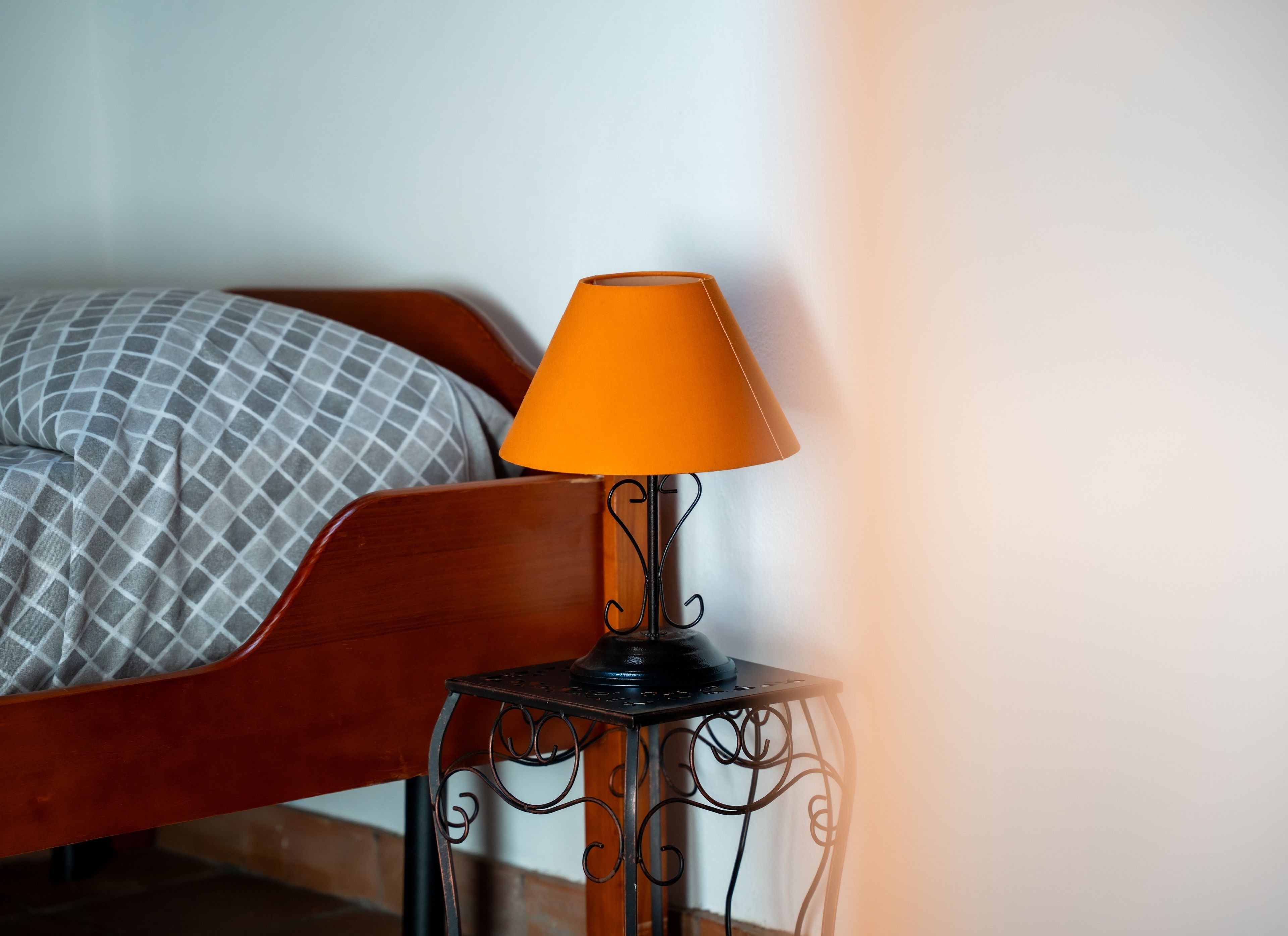 En seng med et mønstret sengetæppe og et natbord med en lampe.
