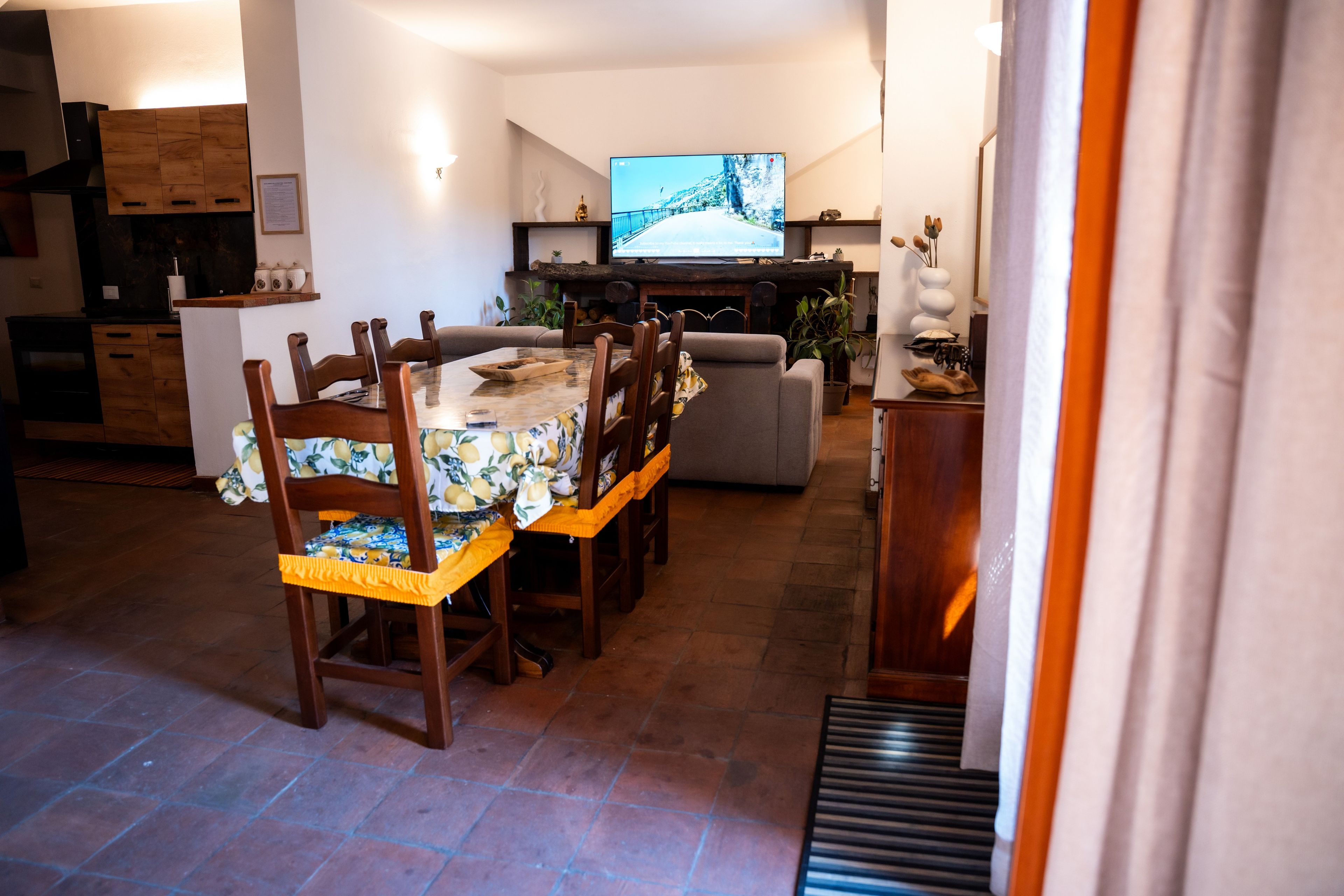 Een eetgedeelte met een lange tafel, stoelen en een televisie op de achtergrond.