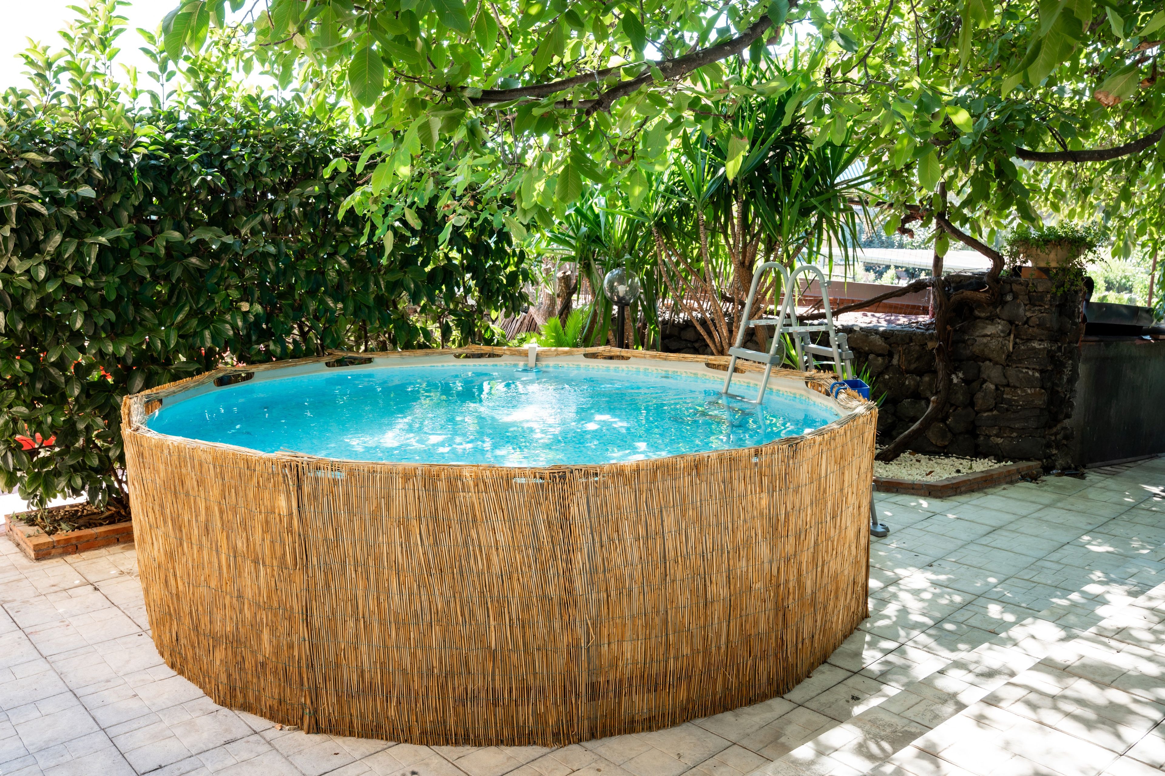 En rund jacuzzi omgivet af et bambushegn, med en stenvæg og grøn bevoksning i baggrunden.
