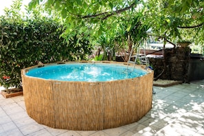 En rund jacuzzi omgivet af et bambushegn, med en stenvæg og grøn bevoksning i baggrunden.