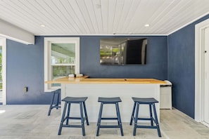 A modern kitchen with a wooden countertop, bar stools, and a large window. - Beach Bliss -waterfront Pool Spa -dock Golf Cart Boat Lift (Anna Maria)