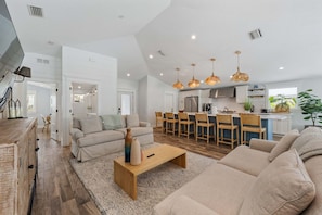 A spacious living area with a sofa, coffee table, and a kitchen in the background. - Beach Bliss -waterfront Pool Spa -dock Golf Cart Boat Lift (Anna Maria)