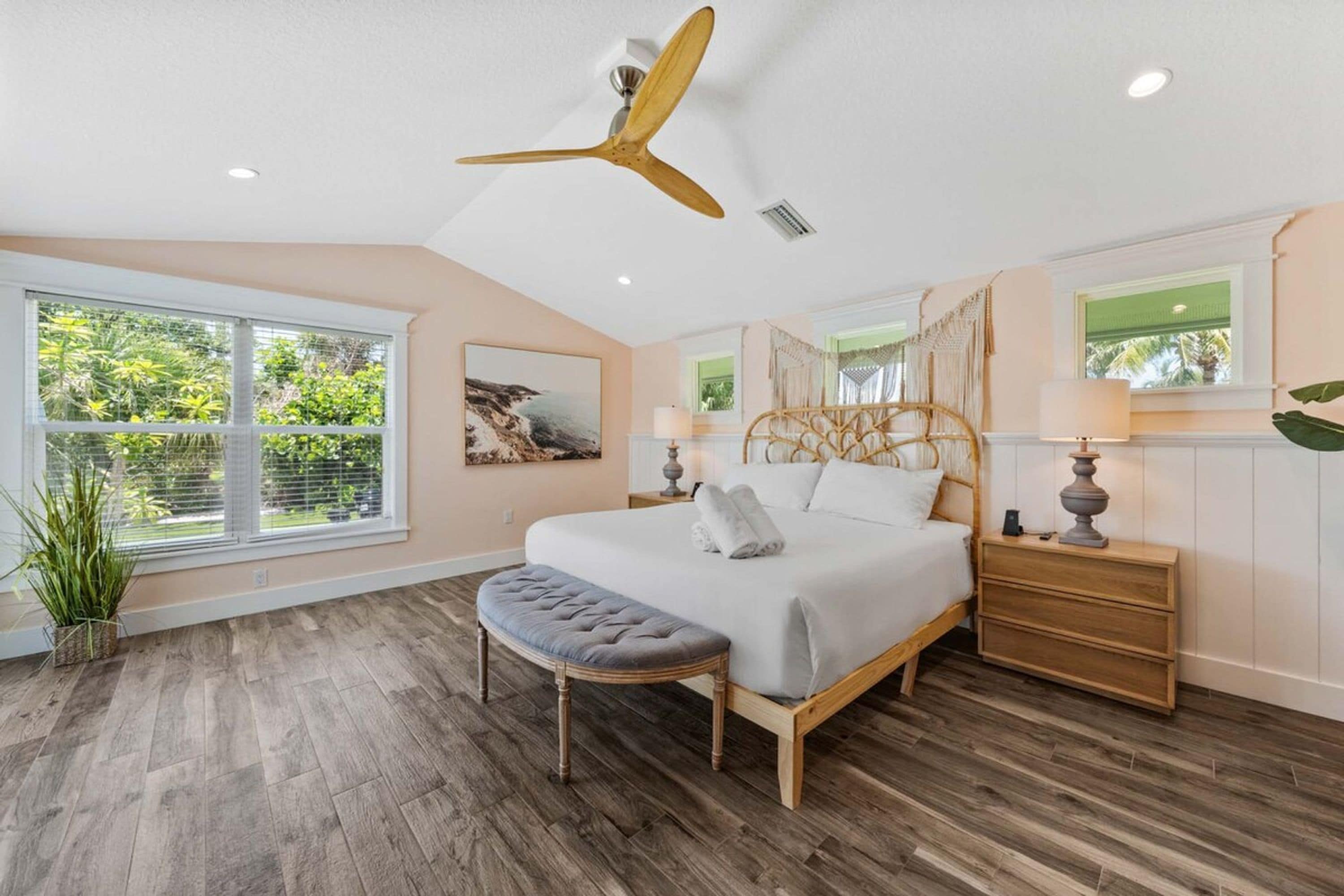 A bedroom with a large bed, a ceiling fan, a window with blinds, and a potted plant.